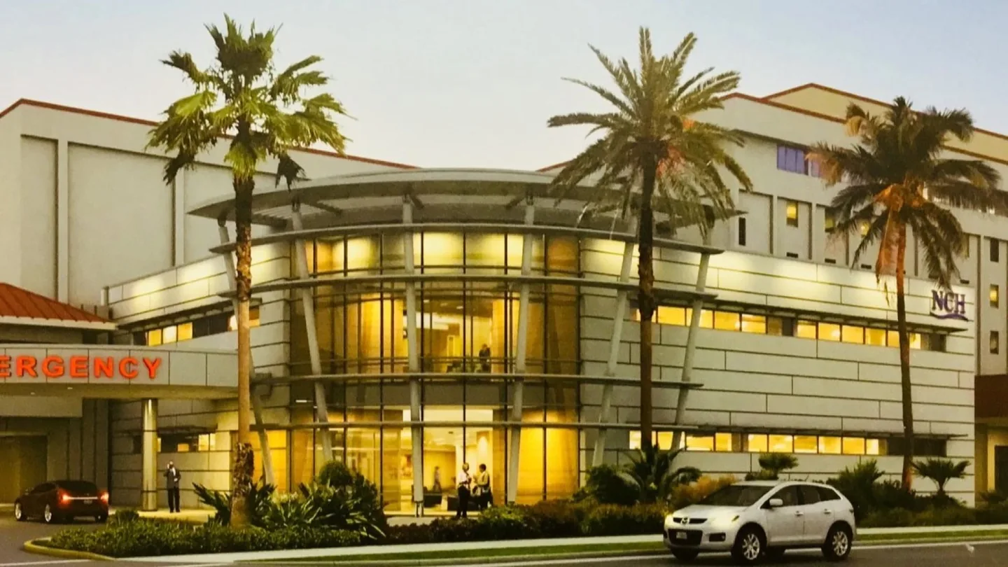 The illuminated emergency entrance at NCH Baker Hospital in Naples, Florida, with palm trees beside the building