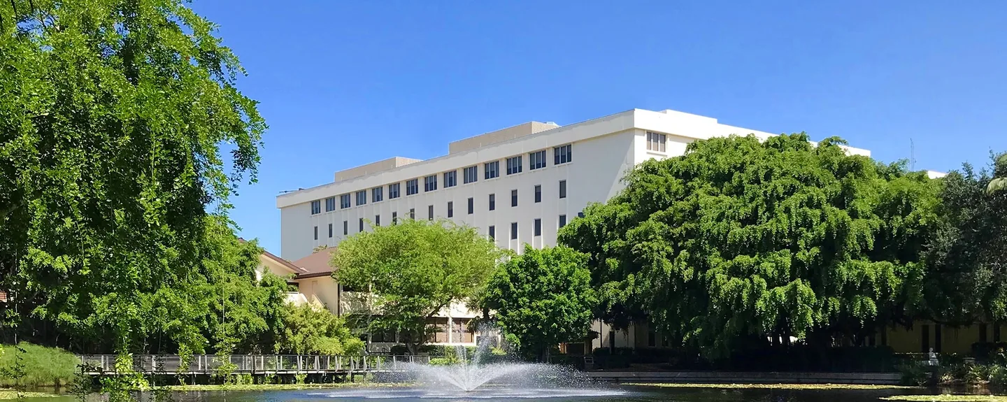 An NCH hospital building framed by trees, with a fountain and walking path in the foreground